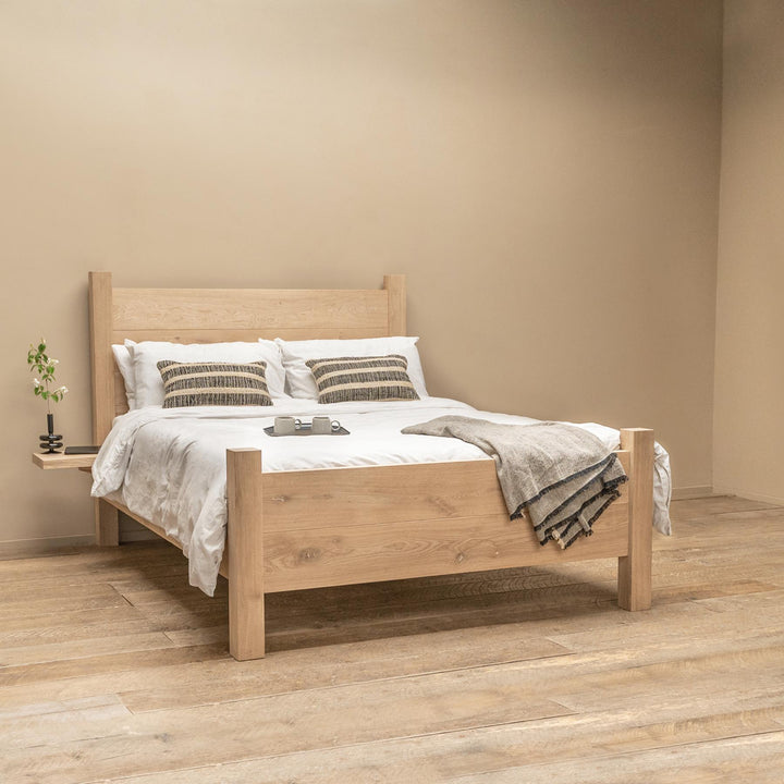 solid oak bed with low footend shown with mattress against a plain off white wall